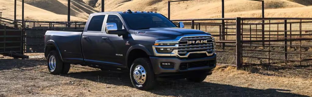 A dark gray RAM 3500 heavy-duty dually pickup truck parked next to a fenced corral on a ranch.