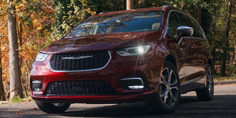 A red minivan is parked on a road surrounded by autumn trees