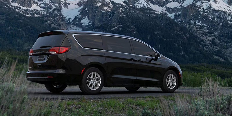A black minivan is parked on a grassy area with snow-covered mountains