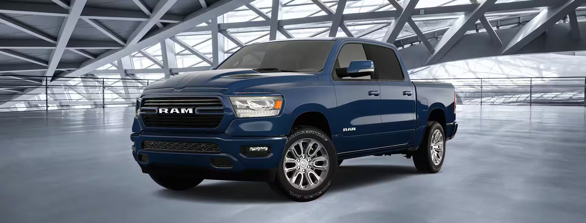 A dark blue 2023 Ram 1500 truck with chrome wheels is parked inside a modern, geometrically designed showroom.