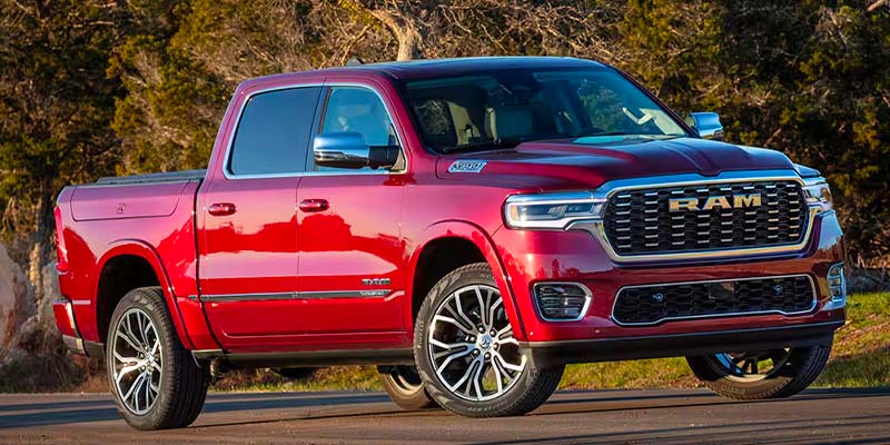 A shiny red Ram pickup truck with chrome accents and large wheels parked on an asphalt road.