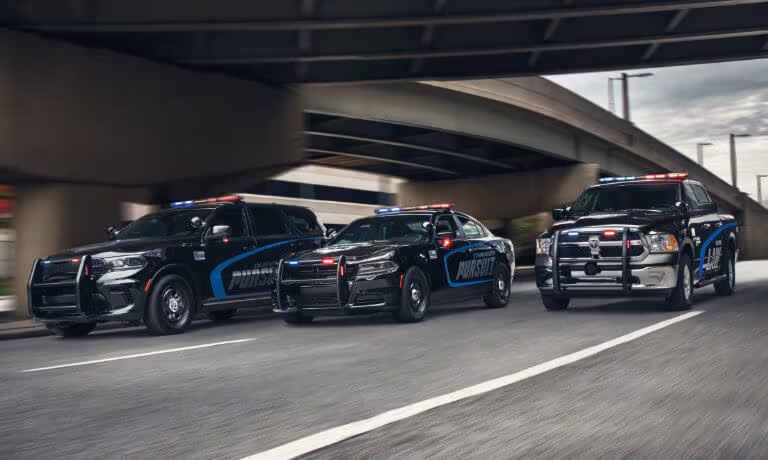 Three black police vehicles driving side by side under an overpass