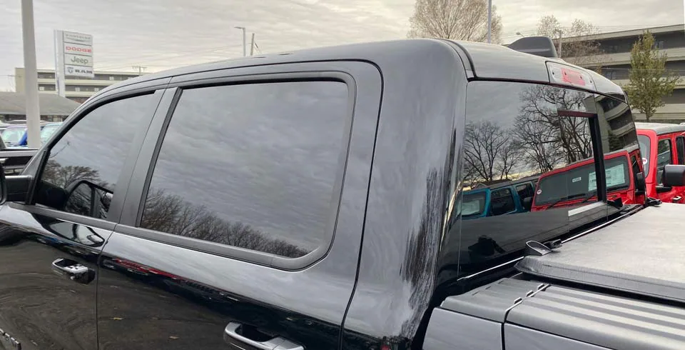 Side view of a black truck with tinted windows, a bed cover, and other vehicles reflected in the windows.