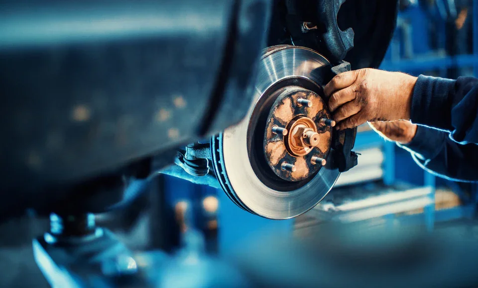 Mechanic's hands working on a vehicle's disc brake rotor and caliper.
