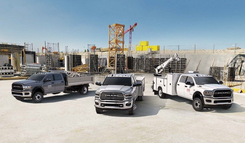 Three Ram heavy-duty trucks parked at a construction site with cranes