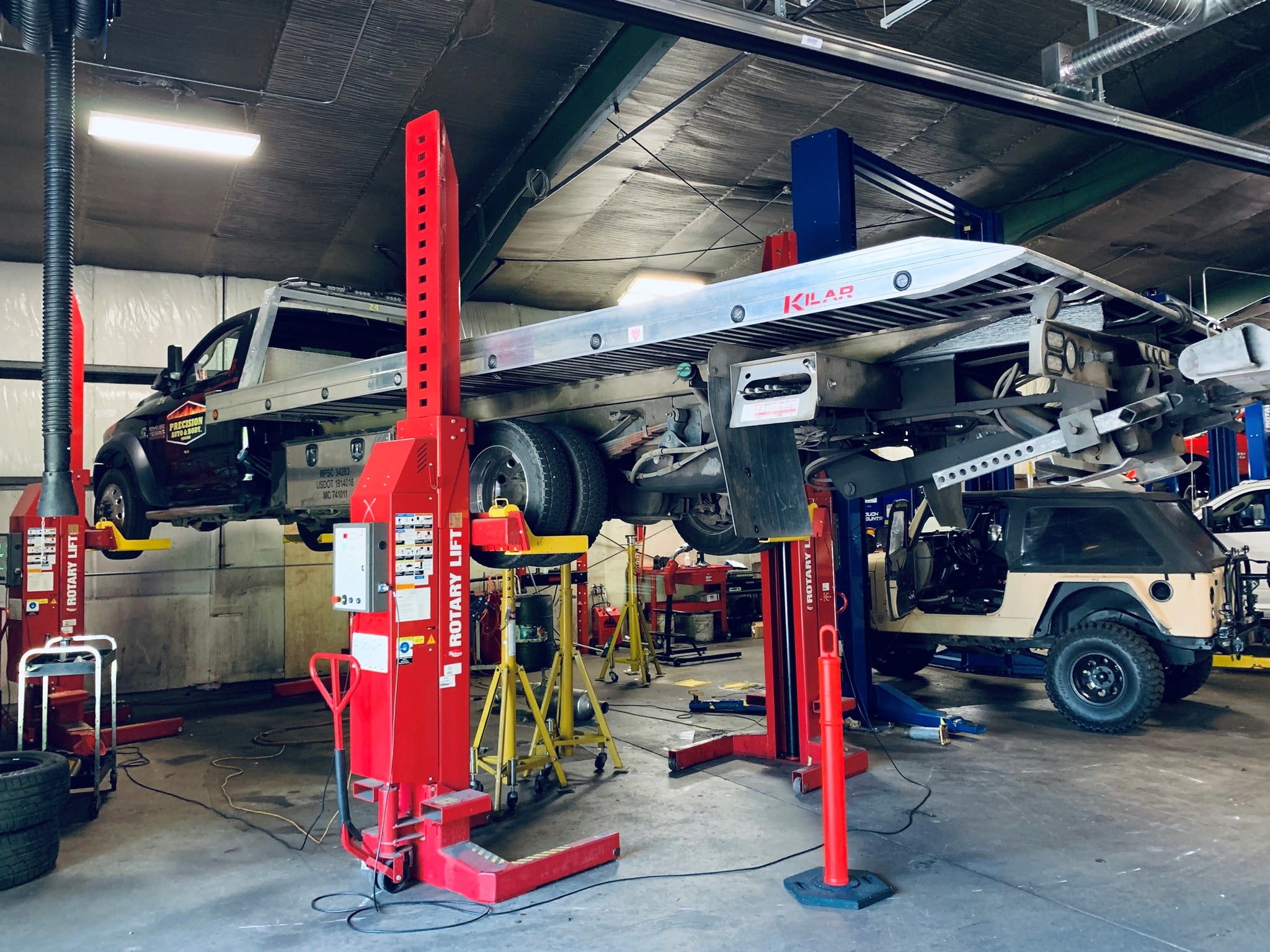A flatbed tow truck raised on red industrial lifts in a garage