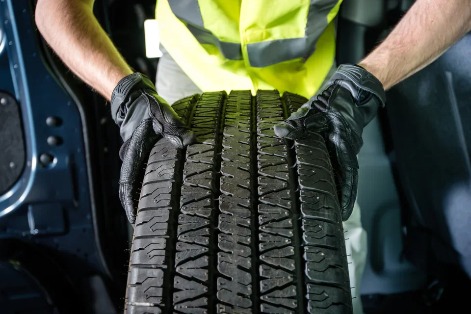 A technician in a safety vest holding a new truck tire