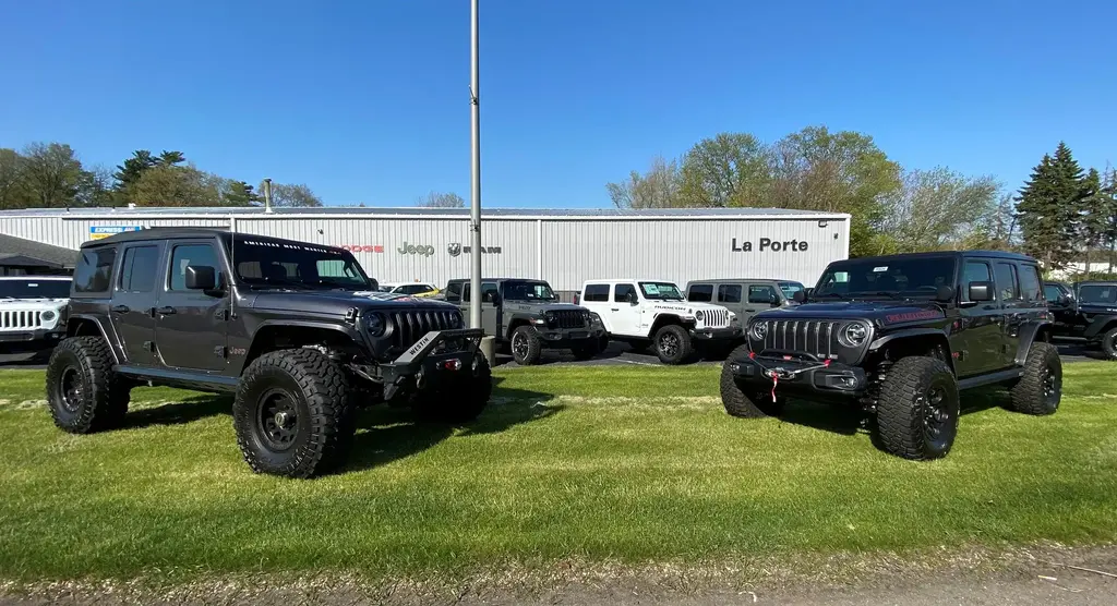 Two large, dark-colored Jeep Wranglers with lifted suspensions and off-road tires on a grassy lawn.