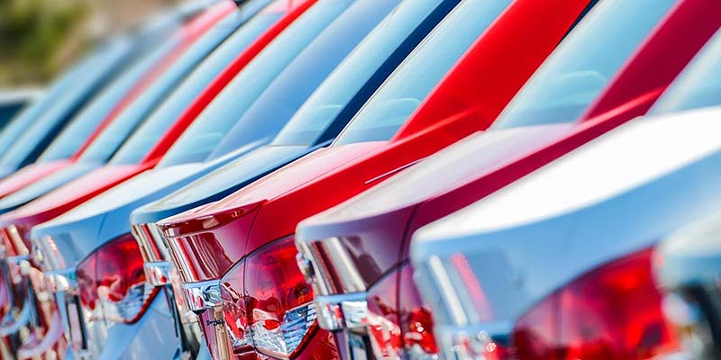 A line of new red and blue cars parked closely together, seen from the rear at an angle.